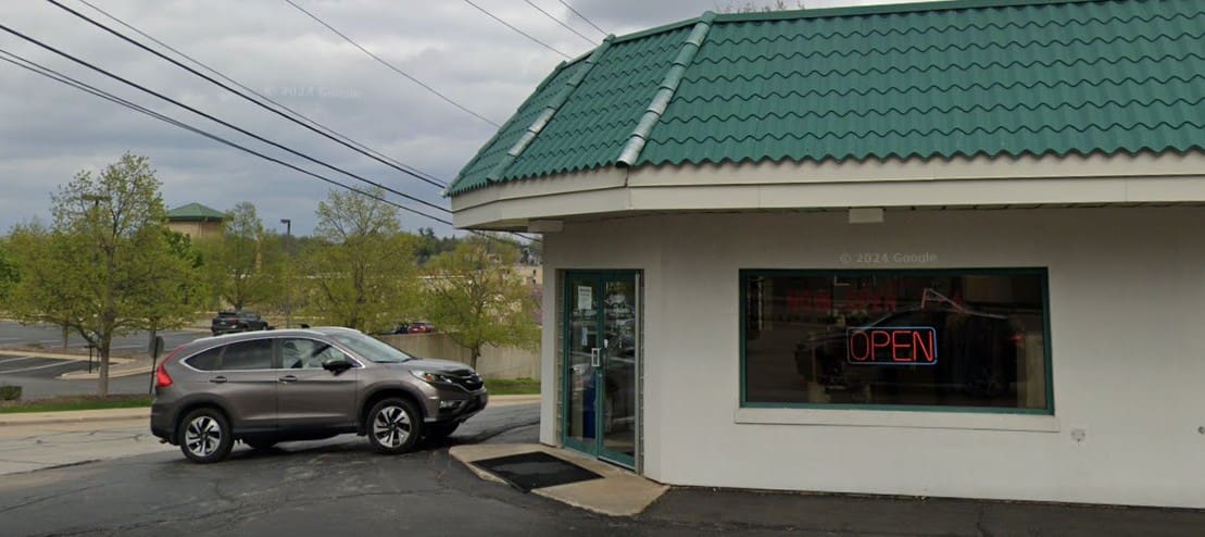 A gray SUV parked outside a building with a green roof; a neon "OPEN" sign is visible in the window.