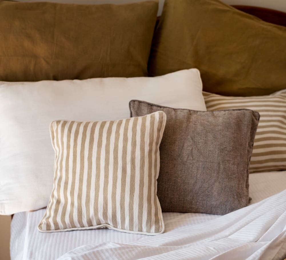 A bed with neatly arranged pillows, including striped, solid beige, solid gray, and striped beige and white designs.