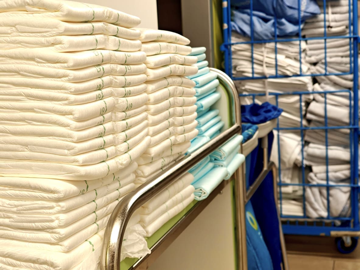 Stacks of folded white and light blue linens arranged on a cart in a healthcare linen room.
